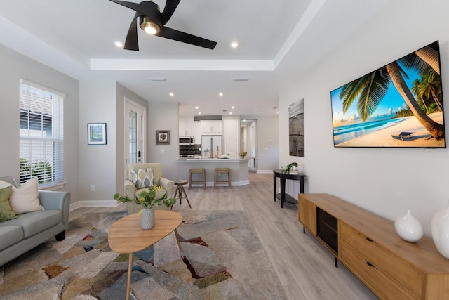 living area with recessed lighting, ceiling fan, a raised ceiling, and light wood-style floors