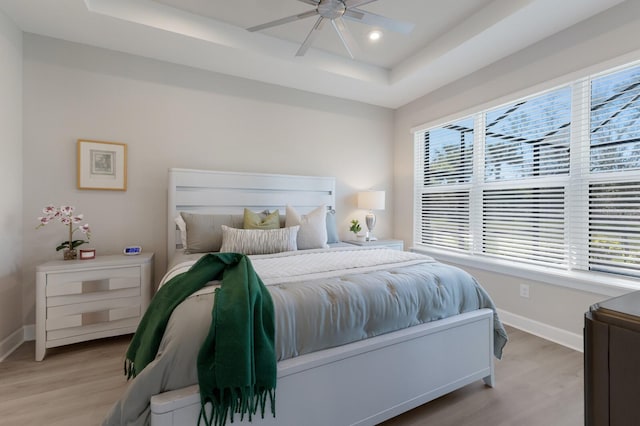 bedroom with a raised ceiling, a ceiling fan, recessed lighting, light wood-style floors, and baseboards