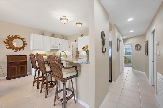 kitchen with white microwave, light stone countertops, light tile patterned flooring, white cabinetry, and a kitchen breakfast bar