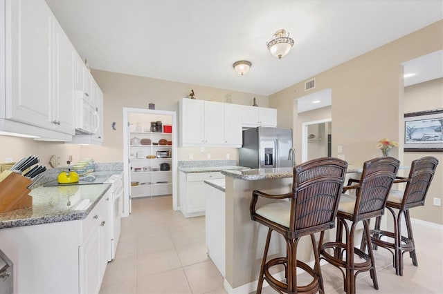 kitchen featuring white microwave, visible vents, a breakfast bar, stainless steel refrigerator with ice dispenser, and stove