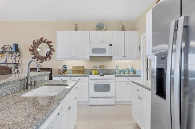 kitchen with white appliances, light stone counters, light tile patterned flooring, a sink, and white cabinets