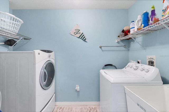 clothes washing area featuring laundry area, a sink, baseboards, and separate washer and dryer