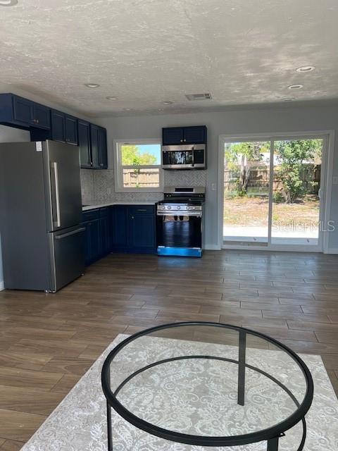 kitchen with decorative backsplash, blue cabinets, dark wood-style flooring, and appliances with stainless steel finishes