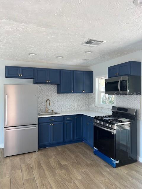 kitchen featuring visible vents, blue cabinetry, stainless steel appliances, and a sink