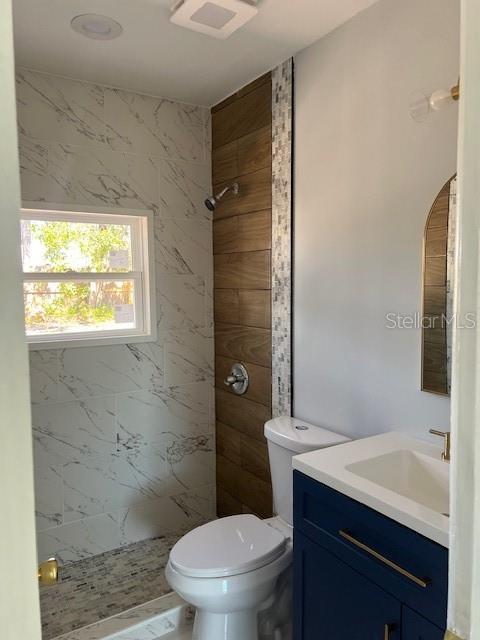 bathroom with visible vents, toilet, tiled shower, and vanity