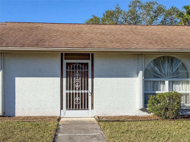 view of exterior entry featuring stucco siding and a shingled roof