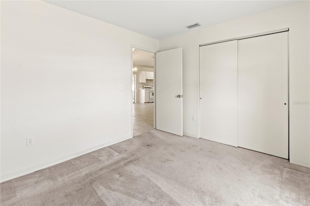 unfurnished bedroom featuring light carpet, visible vents, and a closet