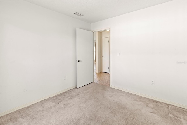 spare room featuring visible vents, baseboards, and light colored carpet