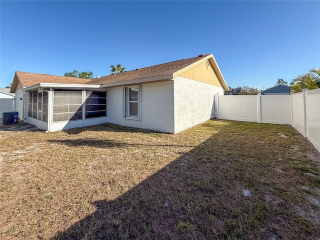 back of house with a fenced backyard, a sunroom, stucco siding, central air condition unit, and a lawn