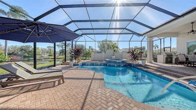 view of pool featuring a ceiling fan, a pool with connected hot tub, a patio, an outdoor kitchen, and a lanai