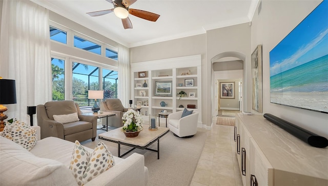 living area featuring a ceiling fan, arched walkways, crown molding, light tile patterned floors, and baseboards