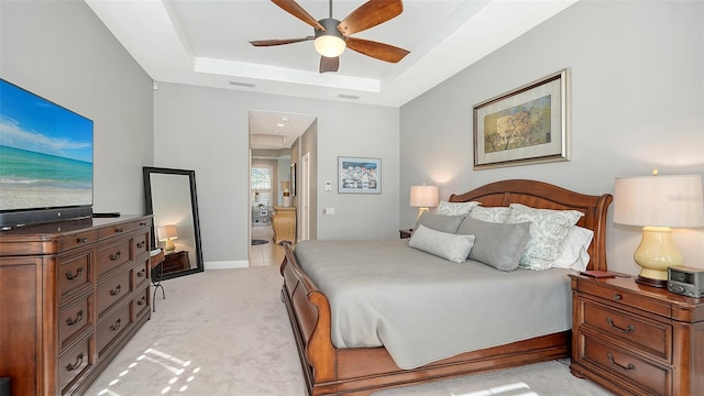 bedroom featuring baseboards, attic access, light carpet, ensuite bath, and a raised ceiling