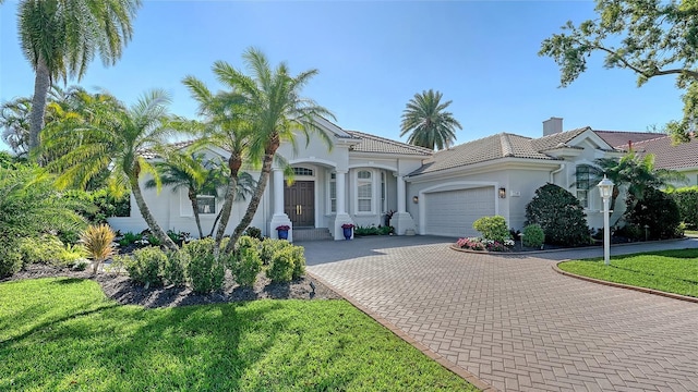 mediterranean / spanish-style house featuring stucco siding, decorative driveway, a garage, a chimney, and a tiled roof