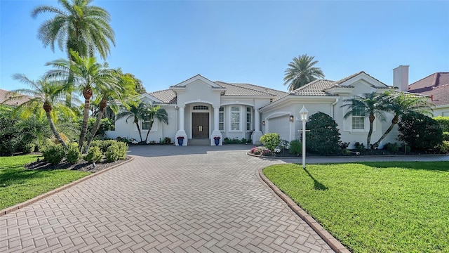 mediterranean / spanish-style home featuring a tiled roof, a front yard, stucco siding, decorative driveway, and an attached garage