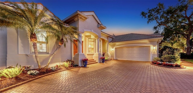 mediterranean / spanish home with stucco siding, a tile roof, decorative driveway, and a garage