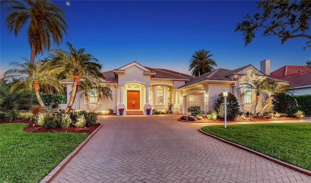 mediterranean / spanish-style house featuring decorative driveway, a tiled roof, an attached garage, and stucco siding