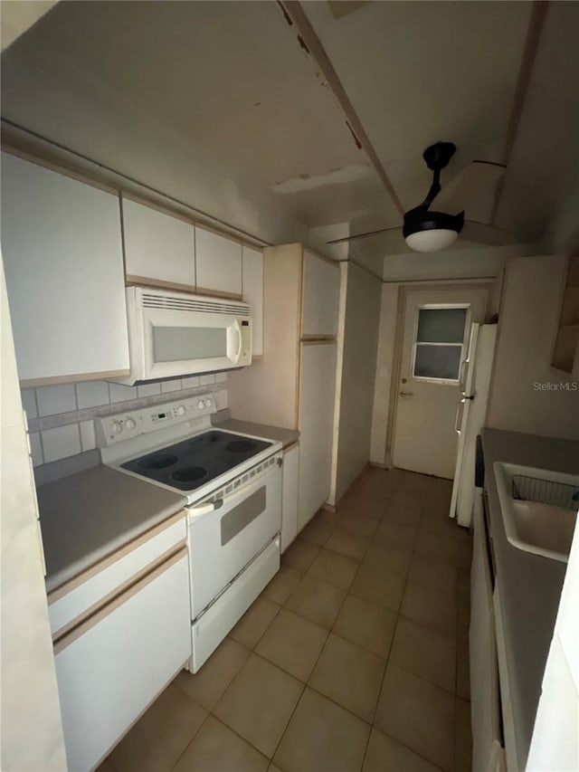 kitchen with light tile patterned floors, decorative backsplash, white cabinets, white appliances, and a sink