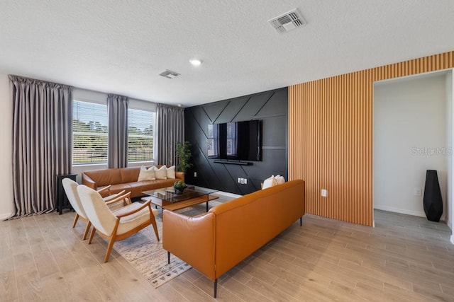 living area featuring light wood-type flooring, visible vents, and a textured ceiling