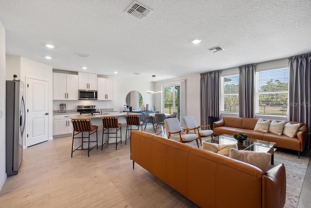 living room featuring visible vents, recessed lighting, a textured ceiling, and light wood-style floors