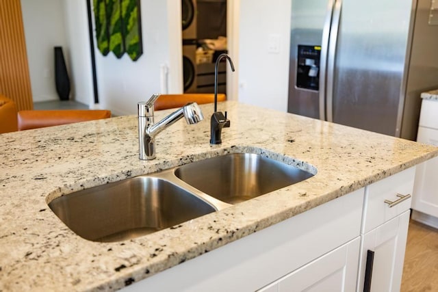 room details featuring white cabinets, light stone countertops, stainless steel refrigerator with ice dispenser, and a sink