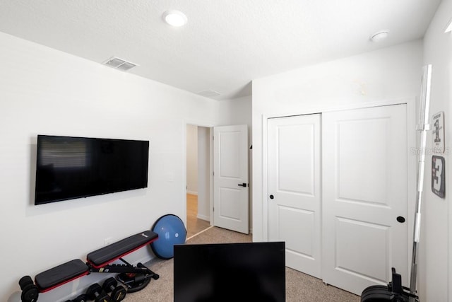 workout area with a textured ceiling, visible vents, and light carpet