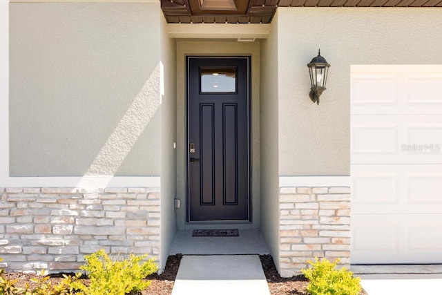 view of exterior entry with a garage, stone siding, and stucco siding