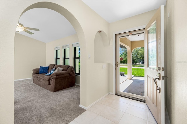 foyer entrance with baseboards, ceiling fan, light carpet, light tile patterned flooring, and arched walkways