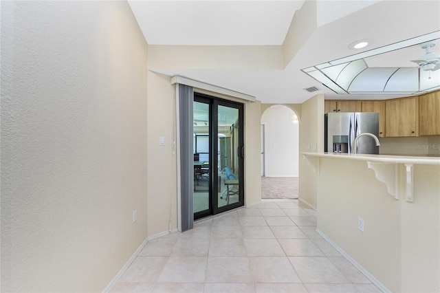 kitchen featuring arched walkways, a breakfast bar, stainless steel fridge with ice dispenser, and light countertops