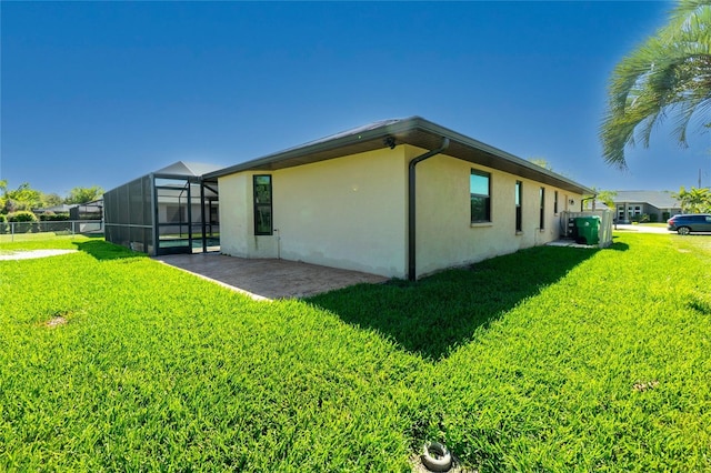 view of side of property featuring fence, glass enclosure, a lawn, stucco siding, and a patio area