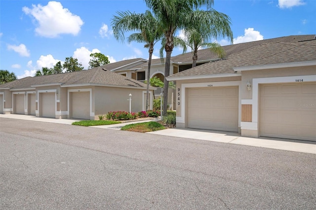 view of property featuring community garages, roof with shingles, and stucco siding