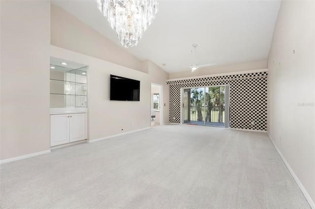 unfurnished living room featuring ceiling fan with notable chandelier, light colored carpet, baseboards, and high vaulted ceiling