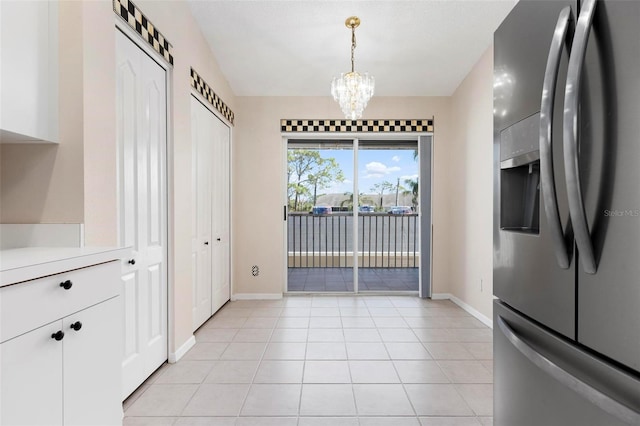 kitchen with light countertops, light tile patterned floors, an inviting chandelier, stainless steel fridge, and white cabinetry