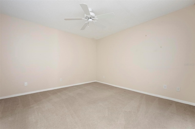 carpeted spare room featuring baseboards and a ceiling fan