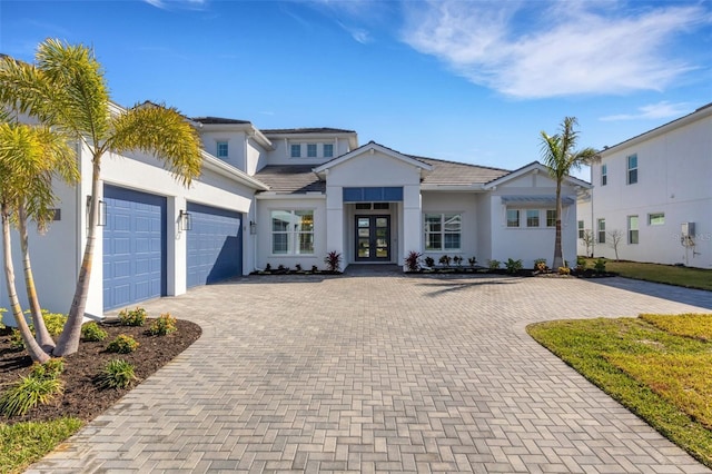 view of front of house with an attached garage, stucco siding, french doors, a tiled roof, and decorative driveway