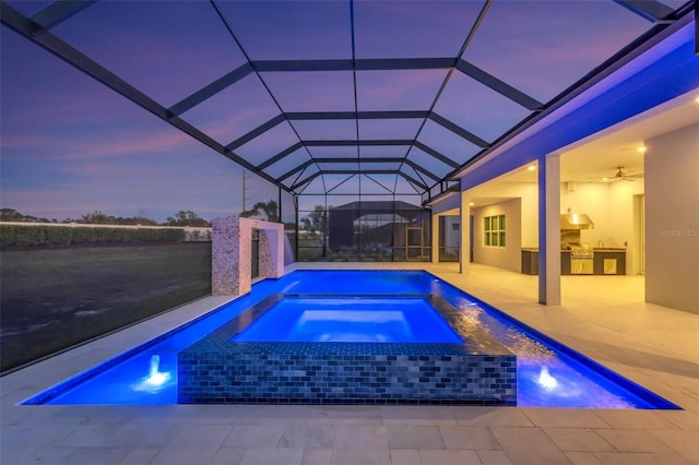 view of swimming pool featuring glass enclosure, exterior kitchen, a pool with connected hot tub, and a patio