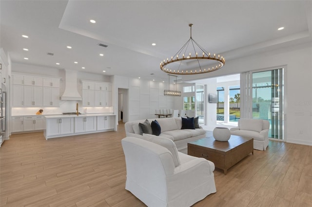 living area featuring light wood-style floors, visible vents, a raised ceiling, and an inviting chandelier