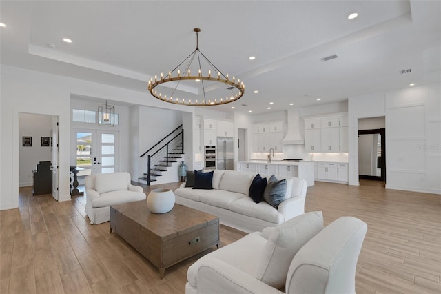 living area with visible vents, a tray ceiling, stairway, light wood finished floors, and a chandelier