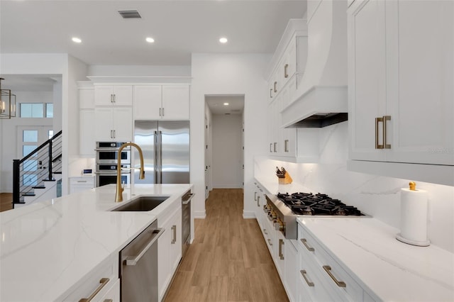 kitchen featuring premium range hood, a sink, tasteful backsplash, appliances with stainless steel finishes, and white cabinets