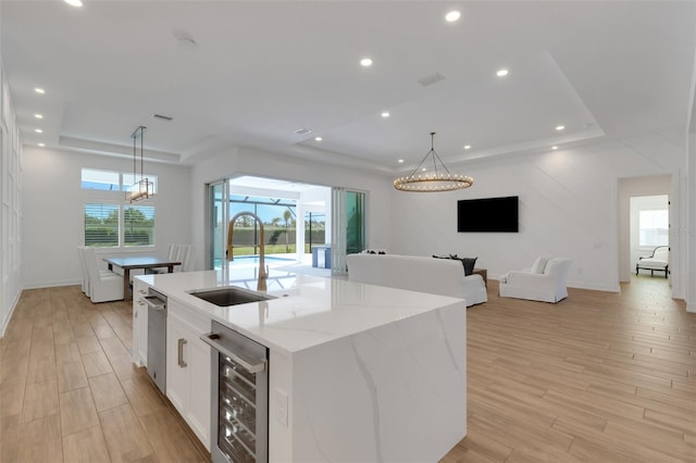 kitchen featuring beverage cooler, a sink, white cabinets, a raised ceiling, and light wood-type flooring