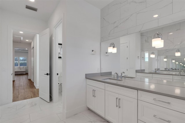 ensuite bathroom featuring visible vents, baseboards, vanity, marble finish floor, and ensuite bath