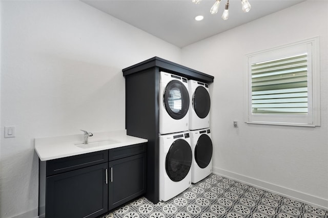 laundry room featuring baseboards, cabinet space, a sink, stacked washer and dryer, and a notable chandelier