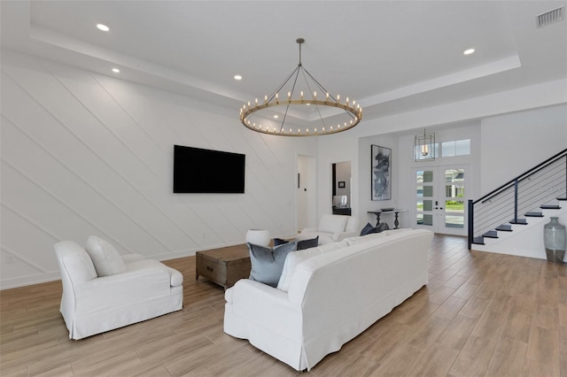 living area with visible vents, a tray ceiling, french doors, an inviting chandelier, and light wood-style floors