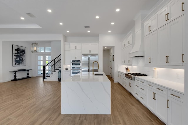 kitchen with a sink, white cabinetry, stainless steel appliances, light wood finished floors, and custom exhaust hood