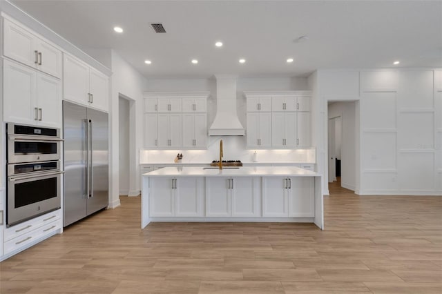 kitchen featuring premium range hood, visible vents, appliances with stainless steel finishes, white cabinets, and light countertops