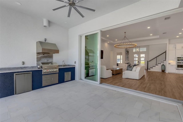 kitchen featuring visible vents, wall chimney range hood, open floor plan, ceiling fan with notable chandelier, and fridge