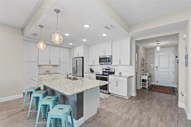 kitchen with visible vents, a sink, stainless steel appliances, light wood-style floors, and a kitchen bar