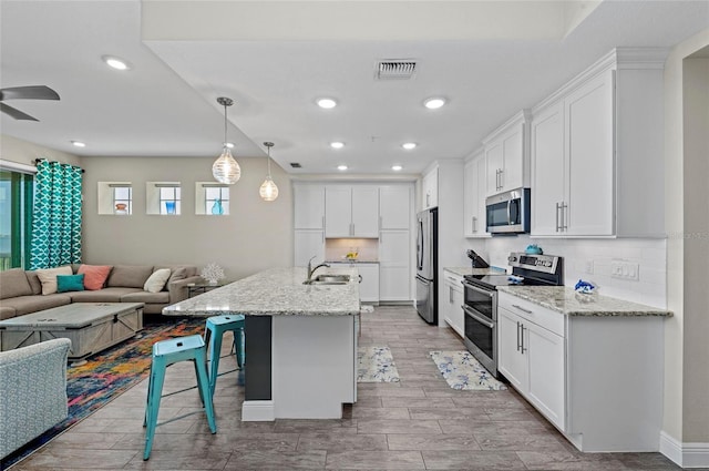 kitchen with visible vents, a breakfast bar, a sink, open floor plan, and stainless steel appliances