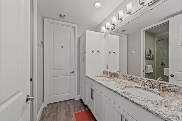 bathroom featuring double vanity, an enclosed shower, wood finished floors, and a sink