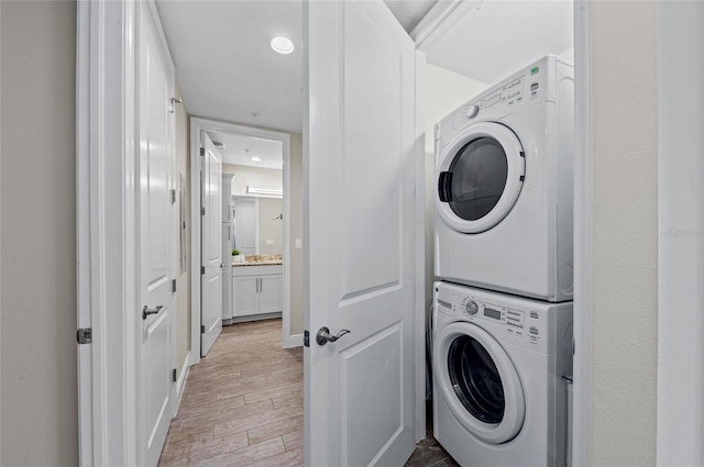 washroom featuring stacked washer / drying machine, baseboards, laundry area, and light wood finished floors