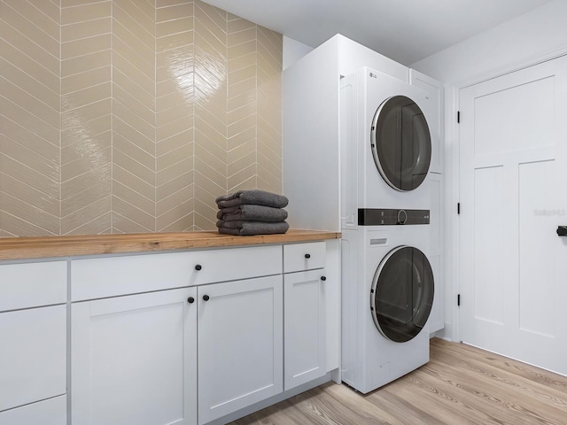 clothes washing area featuring light wood finished floors, laundry area, and stacked washing maching and dryer